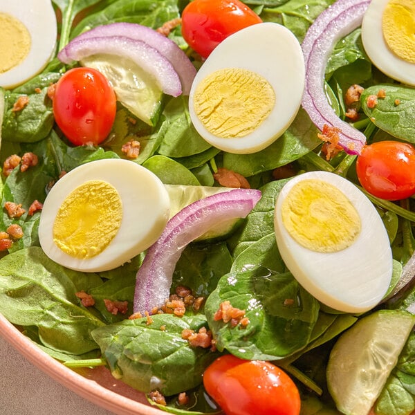 A salad featuring sliced hard cooked eggs, spinach leaves, grape tomatoes, red onion, and bacon bits.