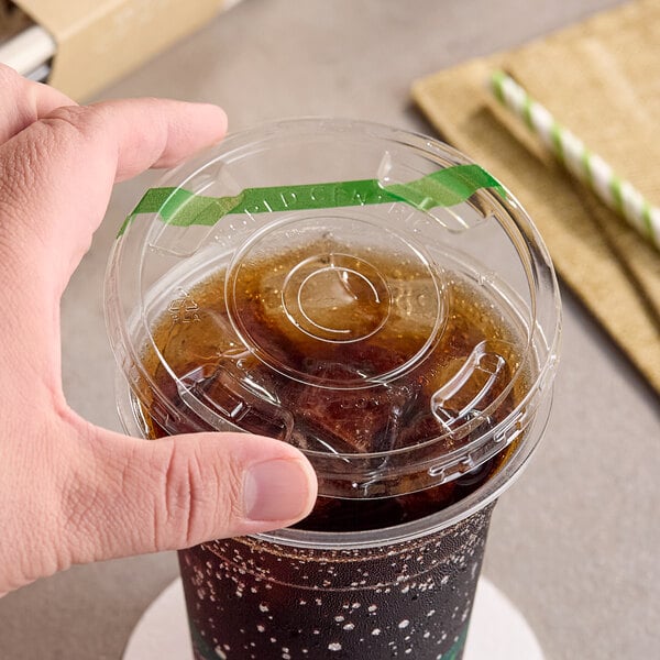 A clear compostable plastic cold cup lid with a straw slot being placed on a cup of iced beverage.
