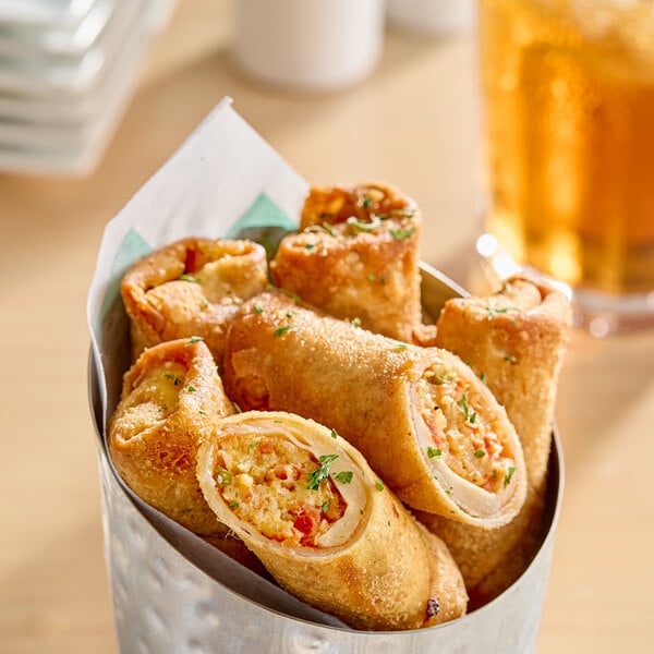 A metal container filled with several golden-brown pizza log egg rolls, some cut open to show a filling of cheese and vegetables.