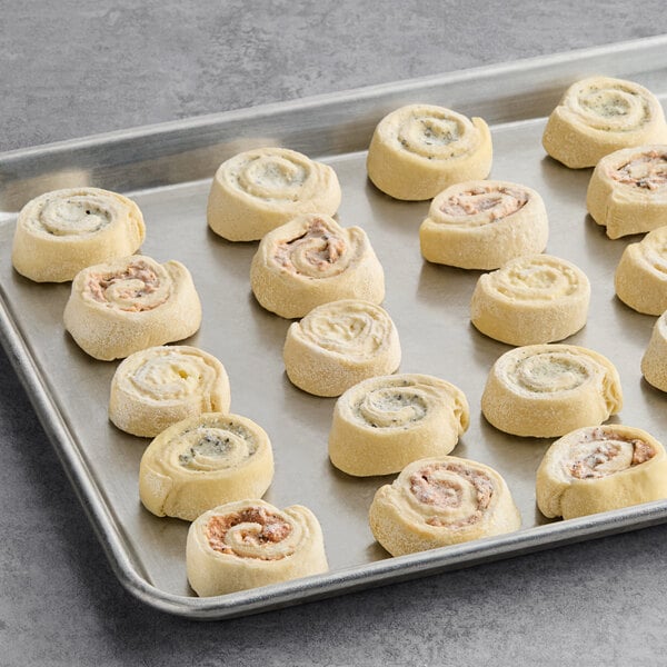 A baking sheet with assorted mini savory pastry swirls arranged in rows.