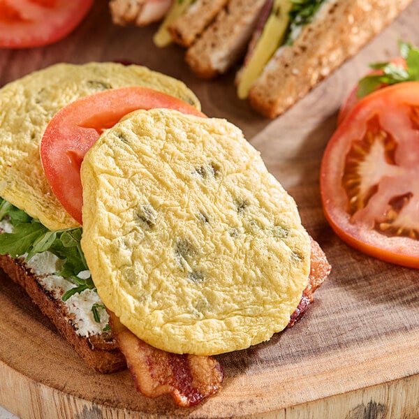 A fully cooked jalapeno scrambled egg patty served on a sandwich with tomato, bacon, greens, and bread.