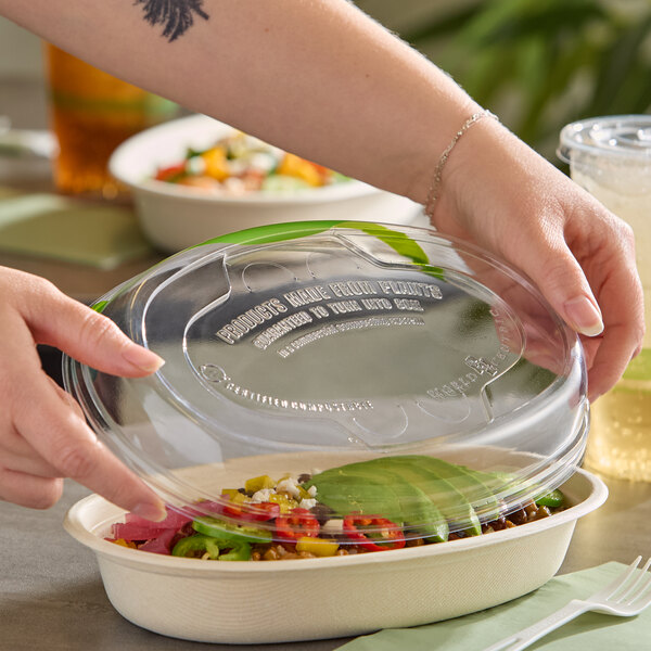 A clear compostable plastic vented lid being placed on a fiber burrito bowl.