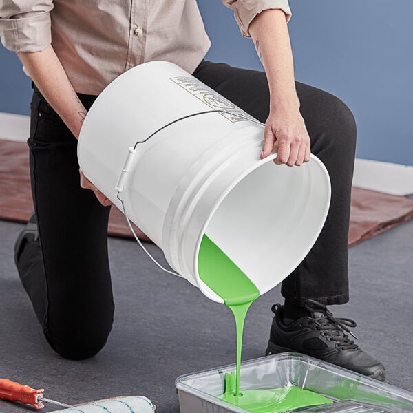 A person pouring green paint into a BWAY white round pail with a metal handle.