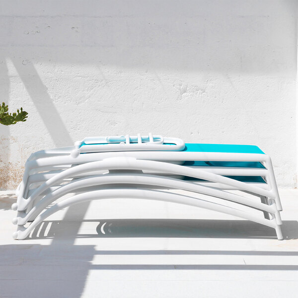 A stack of white adjustable resin chaise lounges with light blue fabric seats.