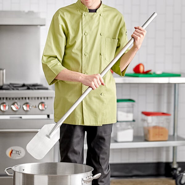 A man in a chef's uniform using a stainless steel paddle to stir a pot on a stove.