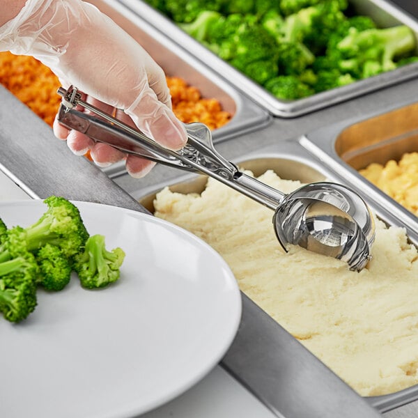 A person holding a Choice Round Stainless Steel Squeeze Handle Disher over a plate of broccoli.