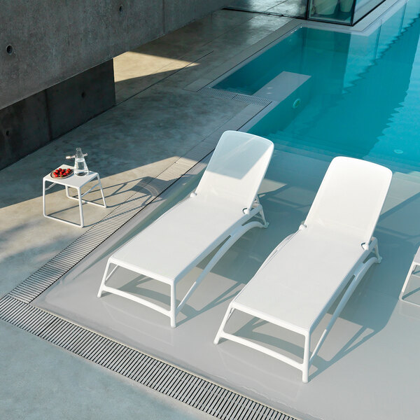 A white resin side table with a tray placed beside a poolside lounge area.