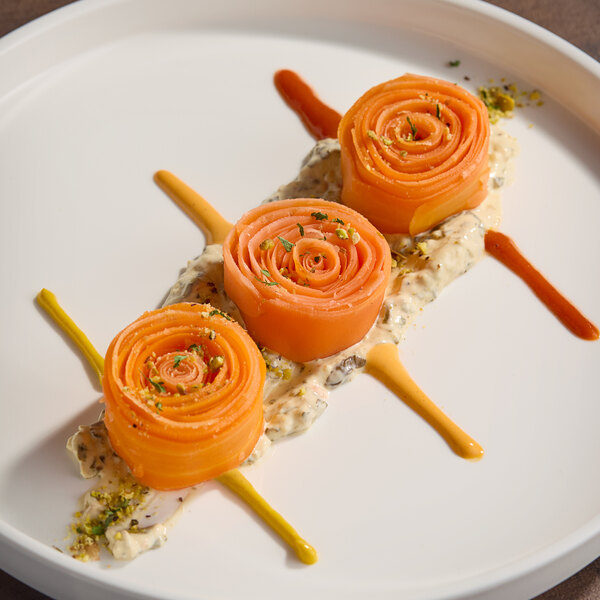 A plate of rolled carrot tagliatelle arranged in a decorative presentation with sauces and garnish.