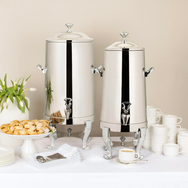 Two Bon Chef stainless steel coffee chafer urns on a table with cups and plates.
