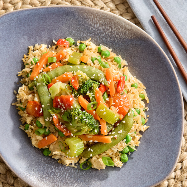 A plate of stir-fried vegetables served over rice, garnished with sesame seeds.