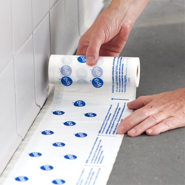 A roll of clear printed overspray protection hand masking film being applied along the edge of a tiled wall and floor.