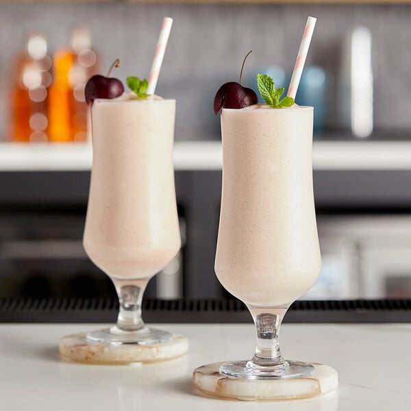 Two glasses of frozen frose with cherries on a bar.