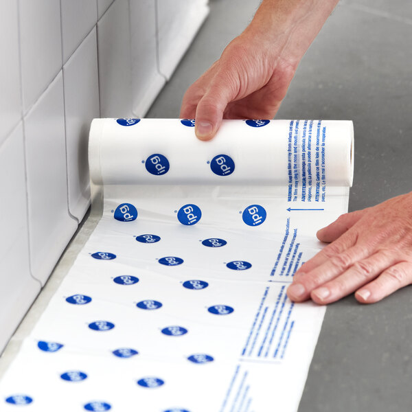 A roll of clear printed overspray protection hand masking film being applied along a tiled wall and floor.