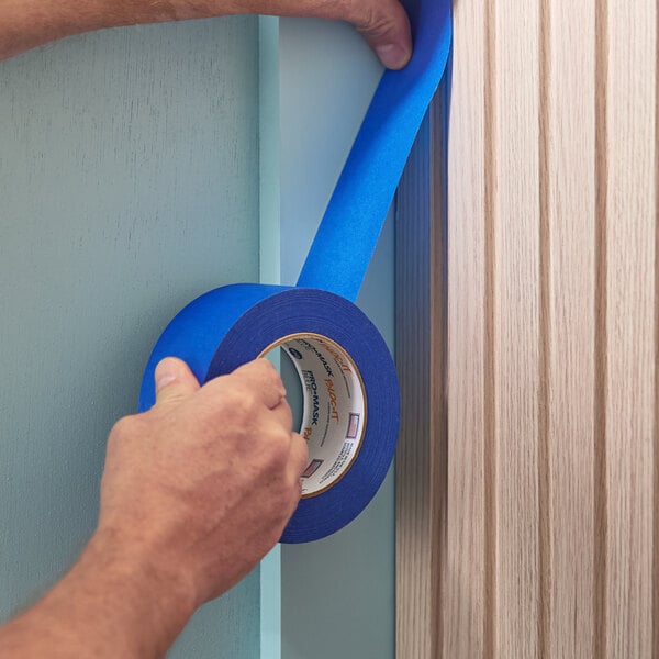 A roll of blue painter's masking tape being applied to a wall corner.