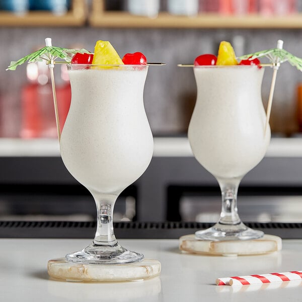 Two glasses of white Pina Colada with fruit on the rim.