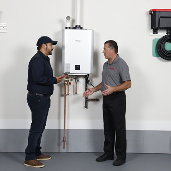 Two men in a professional kitchen standing next to a Rinnai tankless water heater.