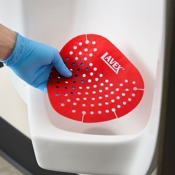 A red vinyl deodorizing urinal screen being placed in a urinal.