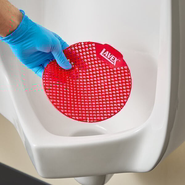 A red vinyl deodorizing urinal screen being placed in a urinal.