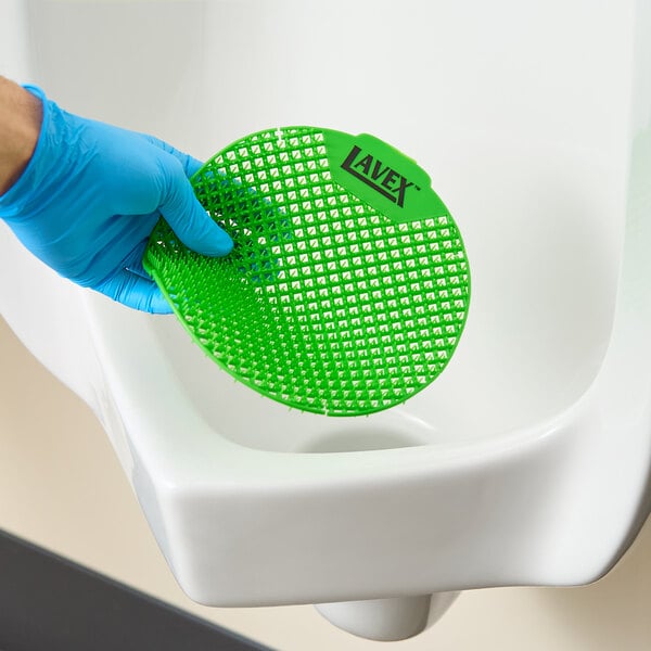 A green vinyl deodorizing urinal screen being placed in a urinal.