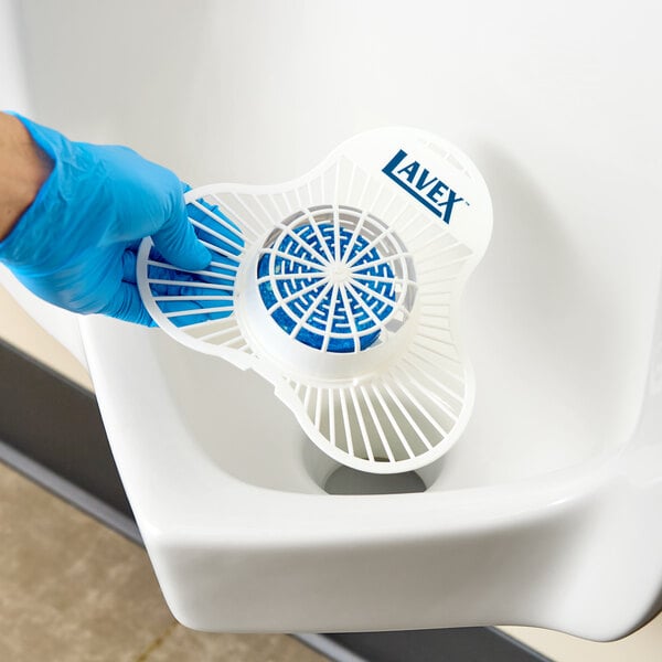 A Lavex deodorizing urinal screen with a citrus scented enzymatic block being placed in a urinal.