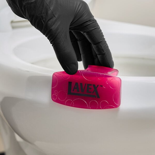 A pink Lavex apple scent toilet bowl clip being placed on the rim of a toilet.