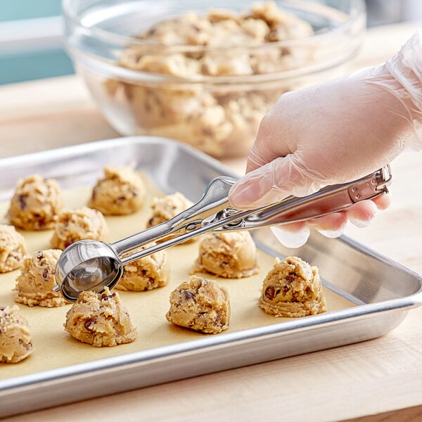 A stainless steel squeeze handle disher being used to portion cookie dough onto a baking sheet.