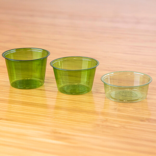Three Eco-Products green PLA plastic portion cups on a wood surface.