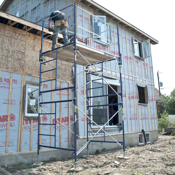 A galvanized steel scaffolding cross brace set up against a house under construction.