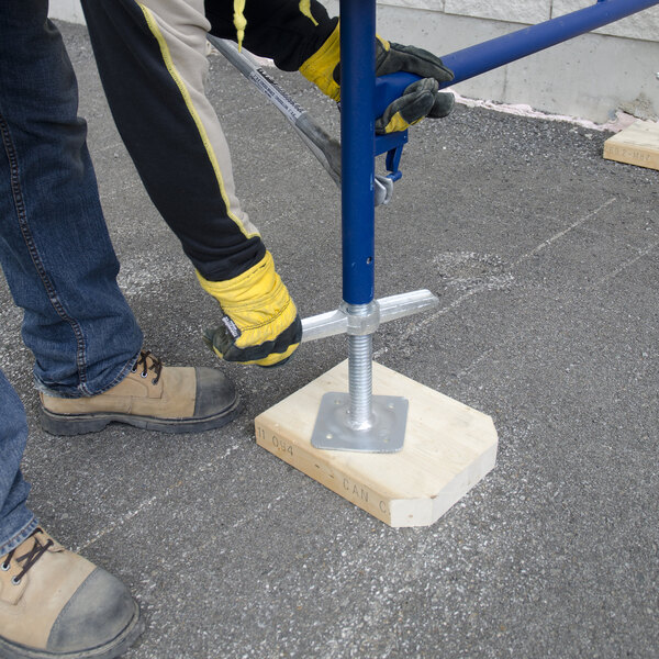 A person adjusting a blue Metaltech SaferStack 24-inch solid galvanized steel adjustable leveling jack with a base plate on a wooden block.