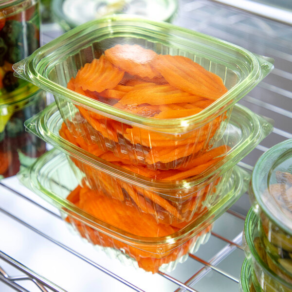A rack with several stacks of Eco-Products green rectangular deli containers filled with carrots.