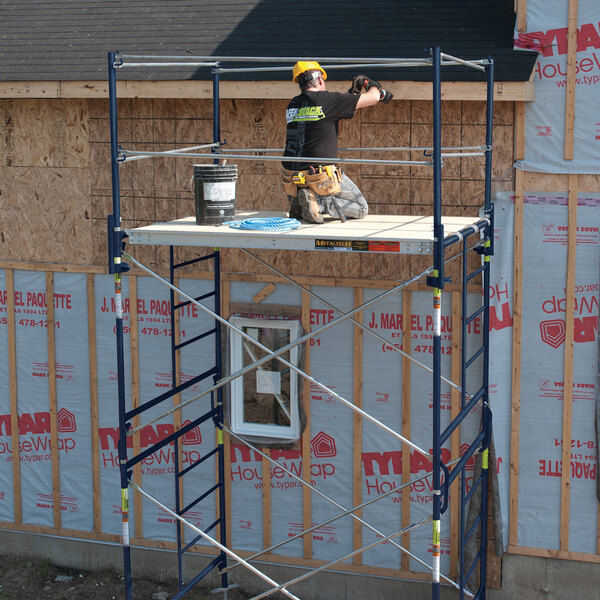 A galvanized steel scaffolding cross brace set up at a construction site with a worker on the platform.