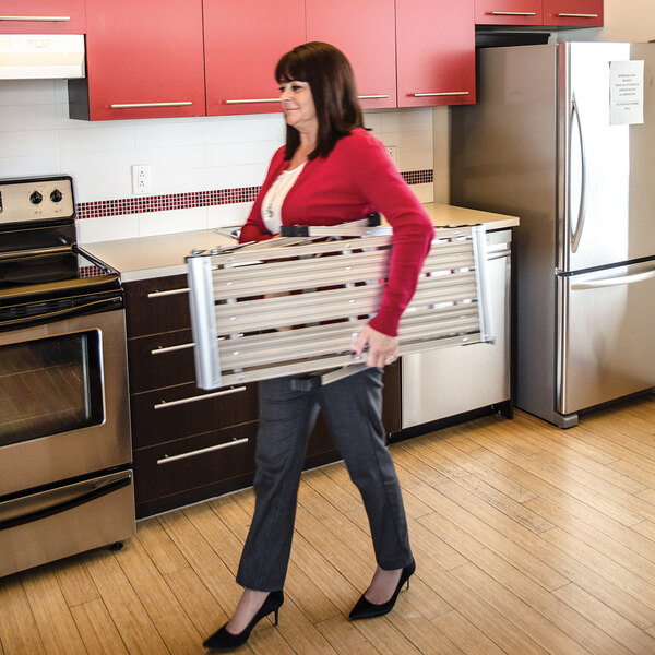 A woman carrying a folded Metaltech Jobsite 39-inch aluminum portable work platform in a kitchen.