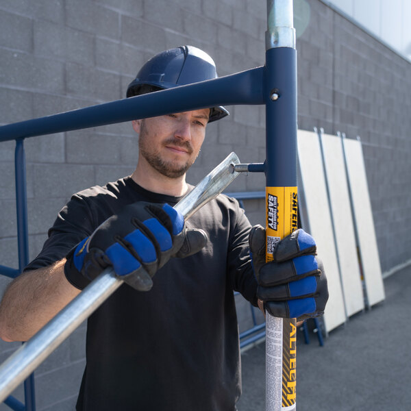 A person wearing safety gear is assembling a Metaltech SaferStack galvanized steel scaffolding cross brace outdoors.
