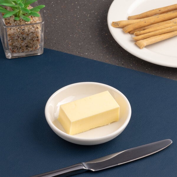A small round white porcelain butter pad holding a rectangular piece of butter.