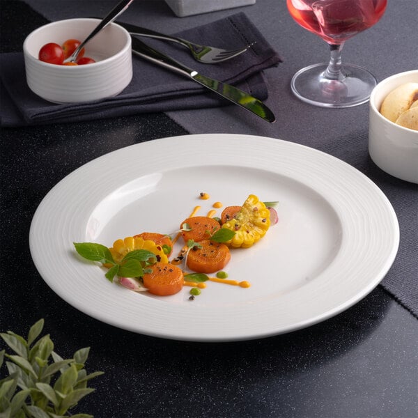 A white round porcelain plate with an embossed wide rim, featuring a small serving of vegetables and garnishes in the center.