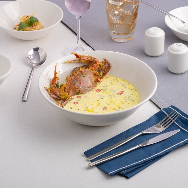 A large warm white porcelain nappie bowl filled with a creamy seafood dish, shown on a set dining table.