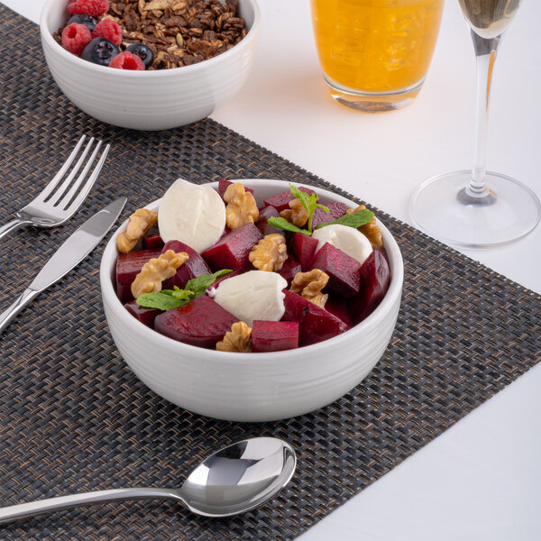 A white embossed porcelain bowl filled with salad, placed on a woven placemat.