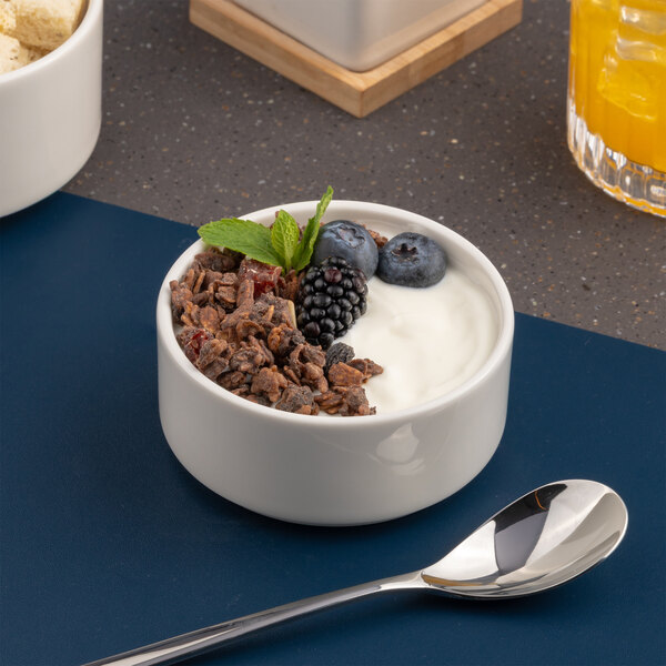 A white porcelain salad bowl filled with yogurt, granola, berries, and a mint garnish.