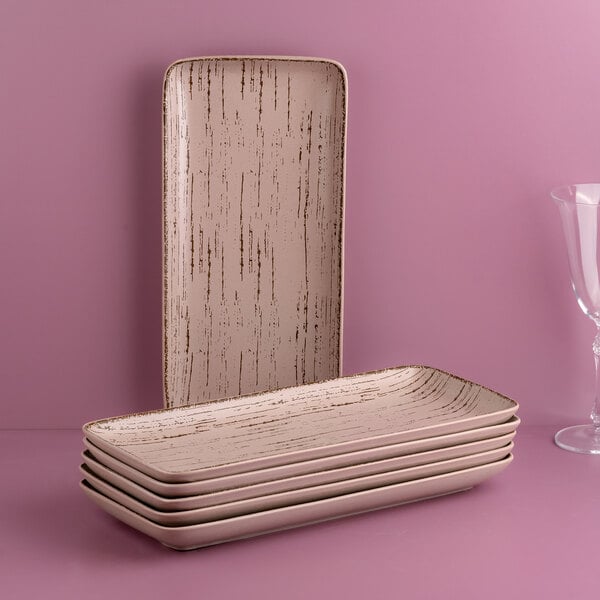A stack of Ariane rectangular porcelain plates on a pink surface.