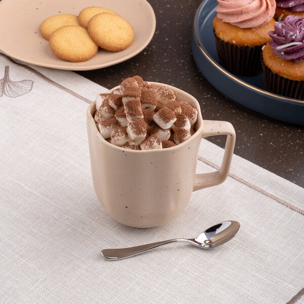 A dark sand dots porcelain mug filled with hot chocolate and marshmallows on a table in a bakery display.
