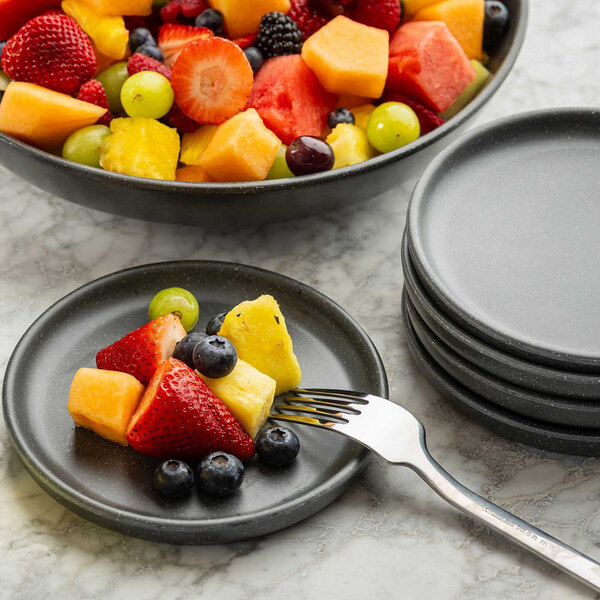 A stack of small, round, speckled gray melamine plates with one plate holding assorted fruit and a fork.