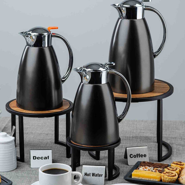 A three-piece set of round acacia wood and steel risers displayed with beverage carafes and food items.