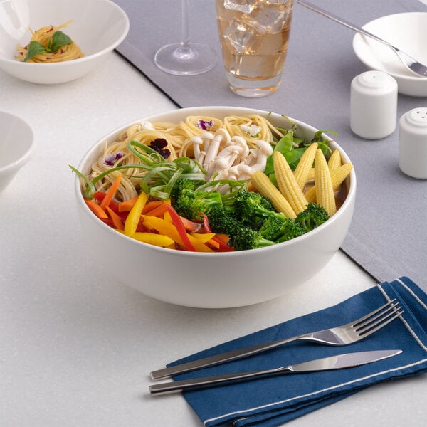 A large warm white porcelain bowl filled with noodles and assorted vegetables.