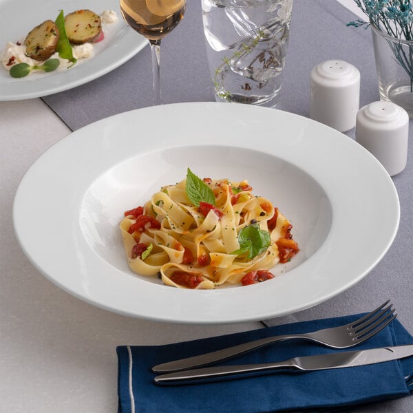 A round, wide-rim deep white porcelain plate with a pasta dish served in the center.