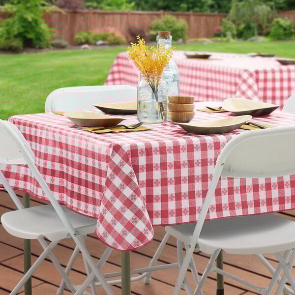A square burgundy and white gingham vinyl table cover with a flannel back, shown on a table set outdoors.