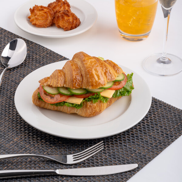 A round white porcelain plate with a wide rim, shown holding a croissant sandwich.