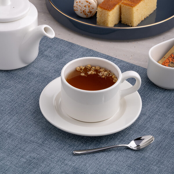 A warm white porcelain tea cup with a matching saucer, filled with tea and placed on a blue placemat.
