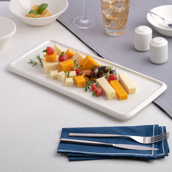 A rectangular warm white porcelain tray with assorted cheeses, nuts, and berries arranged on it.