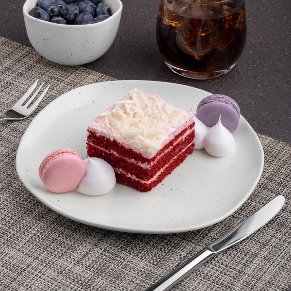 An Ariane porcelain plate with a slice of red velvet cake and a fork on a table.