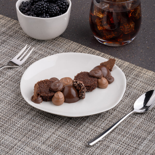 An Ariane Earth porcelain plate with a chocolate dessert and a bowl of blackberries on a table with a glass of juice.